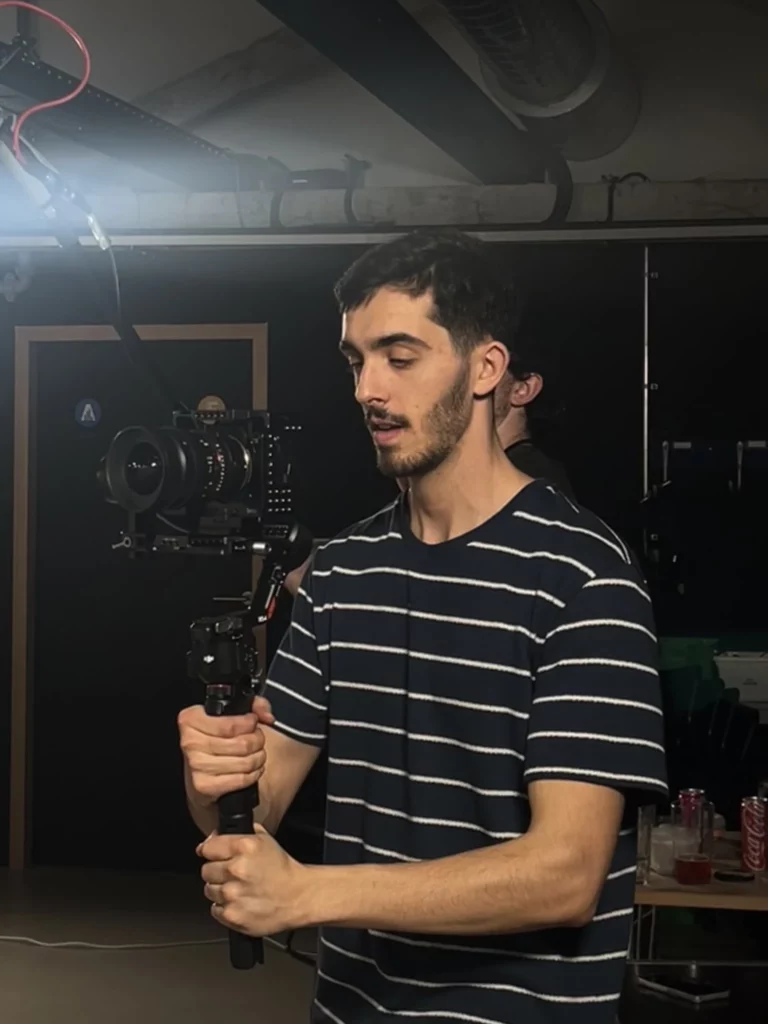 Portrait en plein travail du photographe et vidéaste Mathis DESCOUT concentré, tenant sa caméra professionnelle sur un stabilisateur dans un studio. Les coulisses d'une prestation audiovisuelle réalisée dans le Lot.